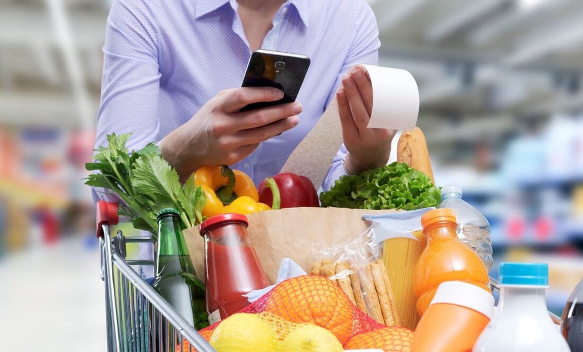Carrito de súper con comida y hombre con celular y ticket