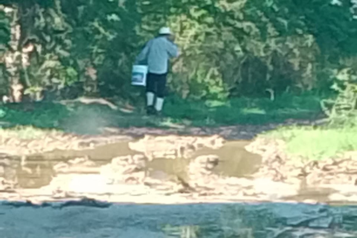 hombre cargando cubeta por camino lodoso