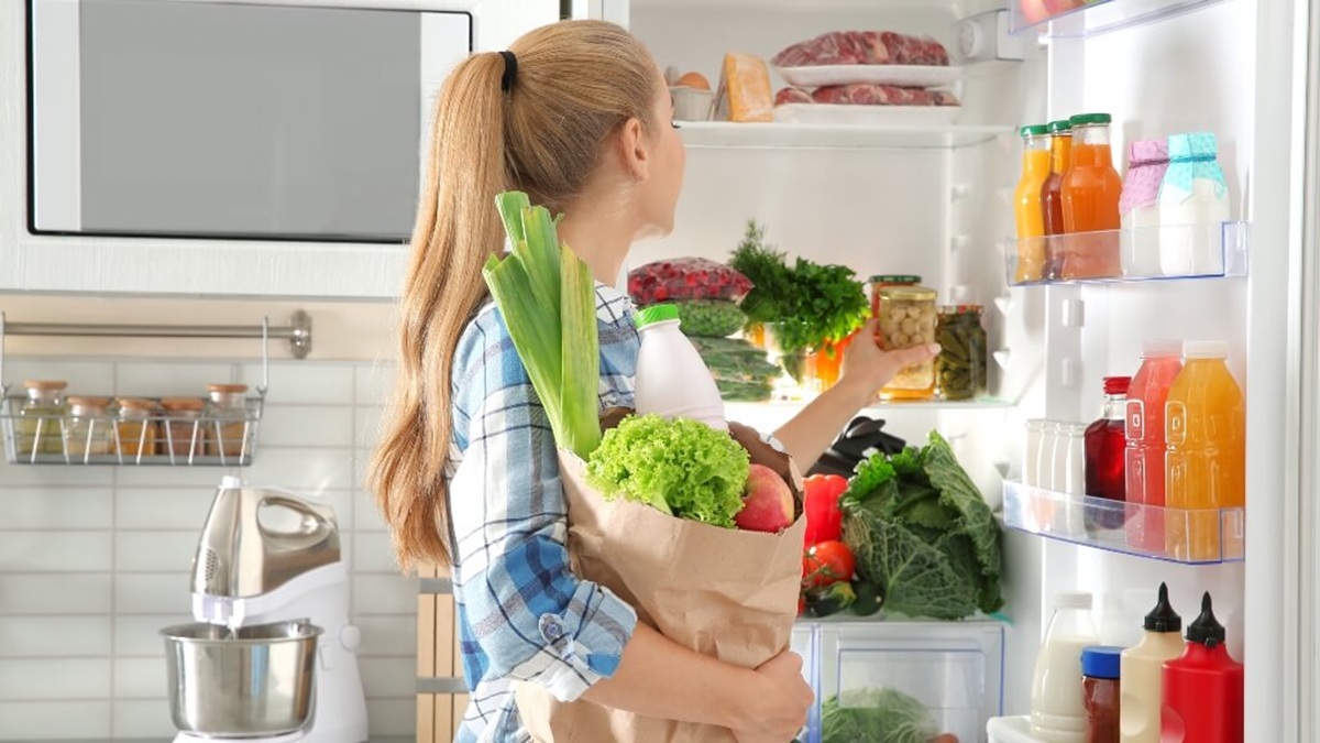 Joven mujer acomodando alimentos en el refrigerador
